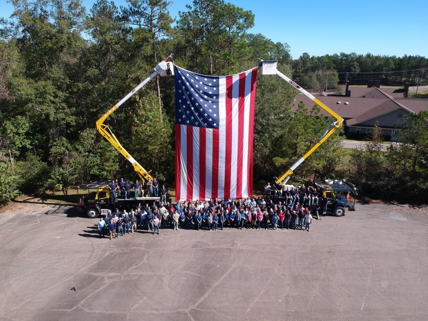 The American Flag being held up by to Pearl River Valley Electric Bucket trucks and a multitude of Pearl River Valley employees surrounding the flag posing for a company picture